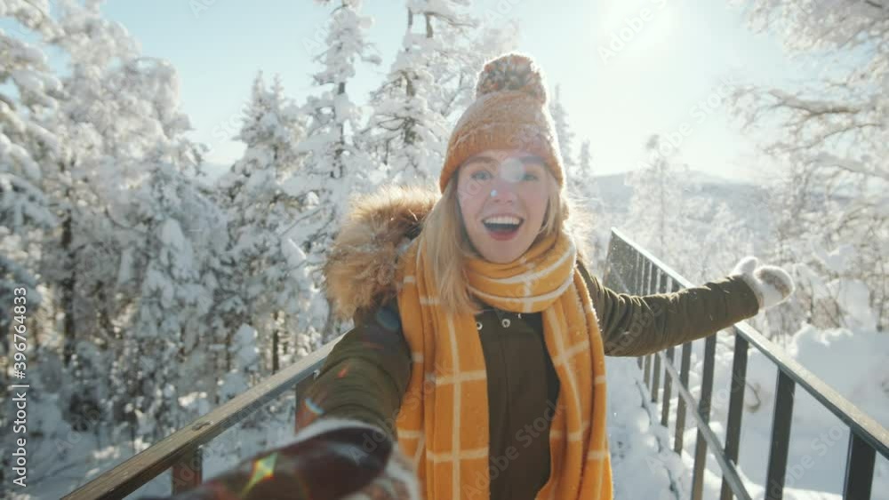 Point of view shot of young pretty woman holding hand of her boyfriend, smiling and talking to him while walking together in park on snowy winter day