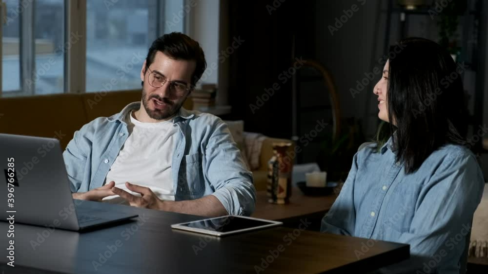 A couple of freelancers in casual wear work remotely in their home office, they use a laptop with internet A couple of freelancers in casual wear work remotely in their home office, they use a laptop with internet