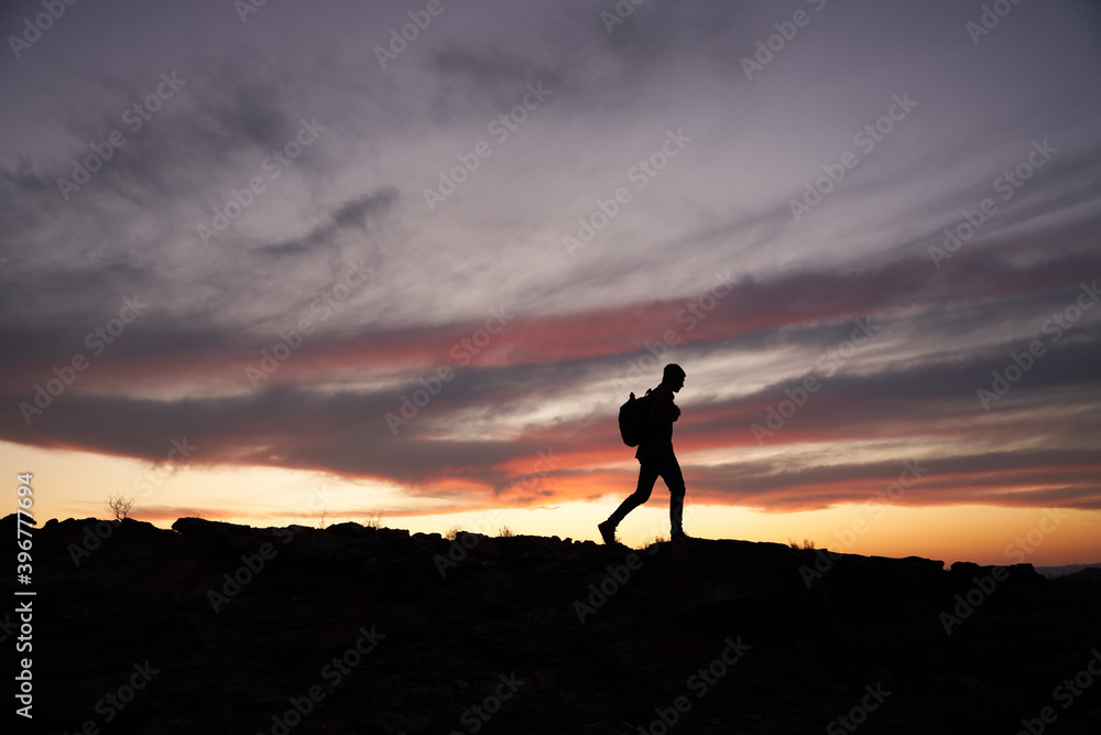 Silhouette of traveller with a backpack climbing up the mountain against beautiful horizon