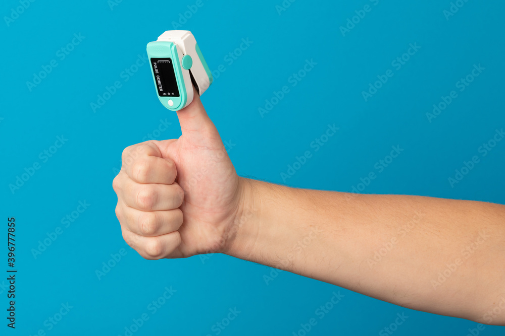 Male hand with an oximeter on the thumb up shows a positive sign..Concept for excellent blood oxygen level, no anxiety due to respiratory failure. Male hand with an oximeter on the thumb up shows a positive sign..Concept for excellent blood oxygen level, no anxiety due to respiratory failure.