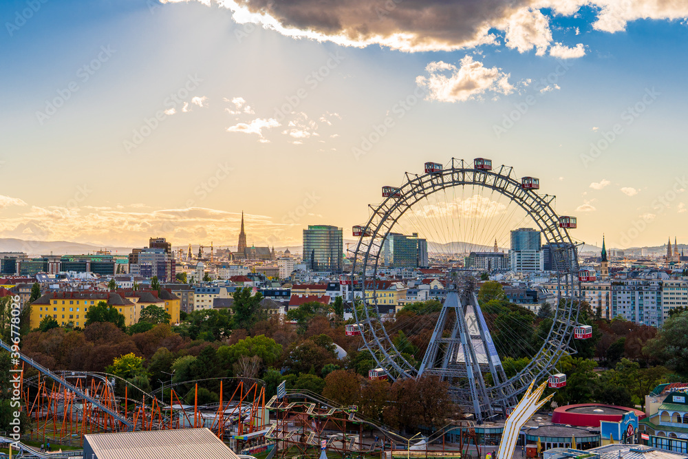 City view of Vienna, Austria, from above at Prater amusement park. Iconic fairy wheel and other amusement rides in the background with the sun peeking out of the clouds. - obrazy, fototapety, plakaty 