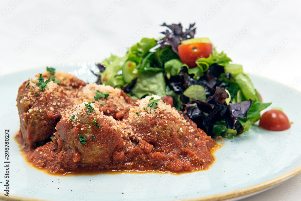 Authentic Italian food shows nutritious Polpettine meatballs covered in marinara sauce and salad on a plate and ready to eat.