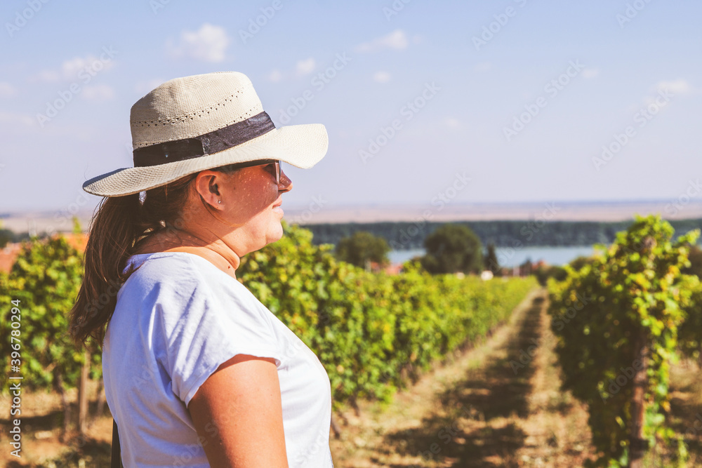 Woman with straw hat relaxing on beautiful summer day at field of vineyards. Summer daylight. Blue sky. Copy-space for message