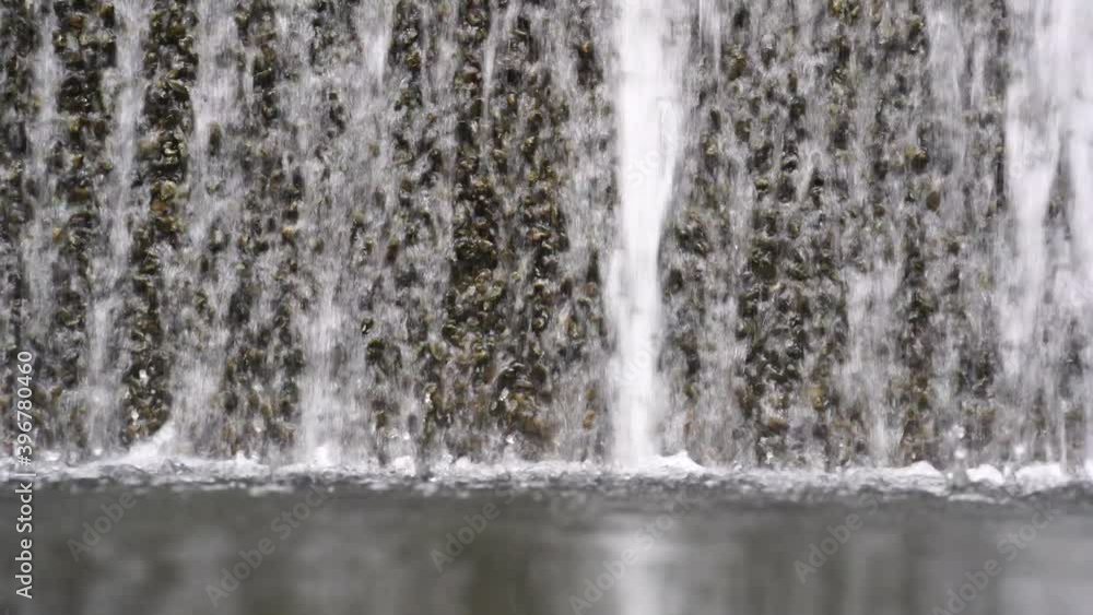 Water falling pouring into a poolside from stone wall, close up. Background with running water. Waterfall fountain stri and spray drops stone surface. Water falling pouring into a poolside from stone wall, close up. Background with running water. Waterfall fountain stri and spray drops stone surface.