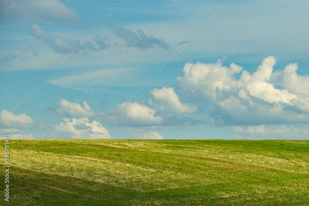 Blue sky with white clouds and a sunny green field in the lower third of the image Blue sky with white clouds and a sunny green field in the lower third of the image