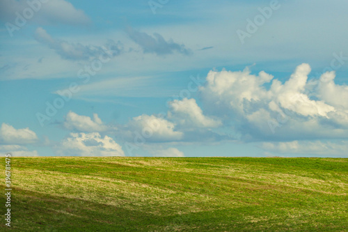 Blue sky with white clouds and a sunny green field in the lower third of the image