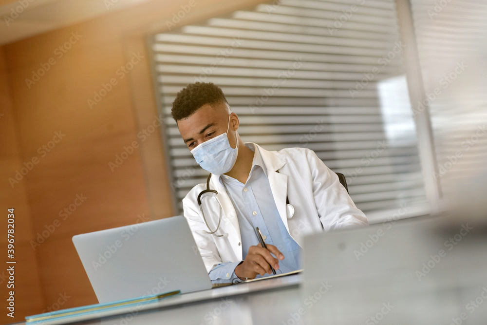 Young doctor working on laptop with face mask Young doctor working on laptop with face mask