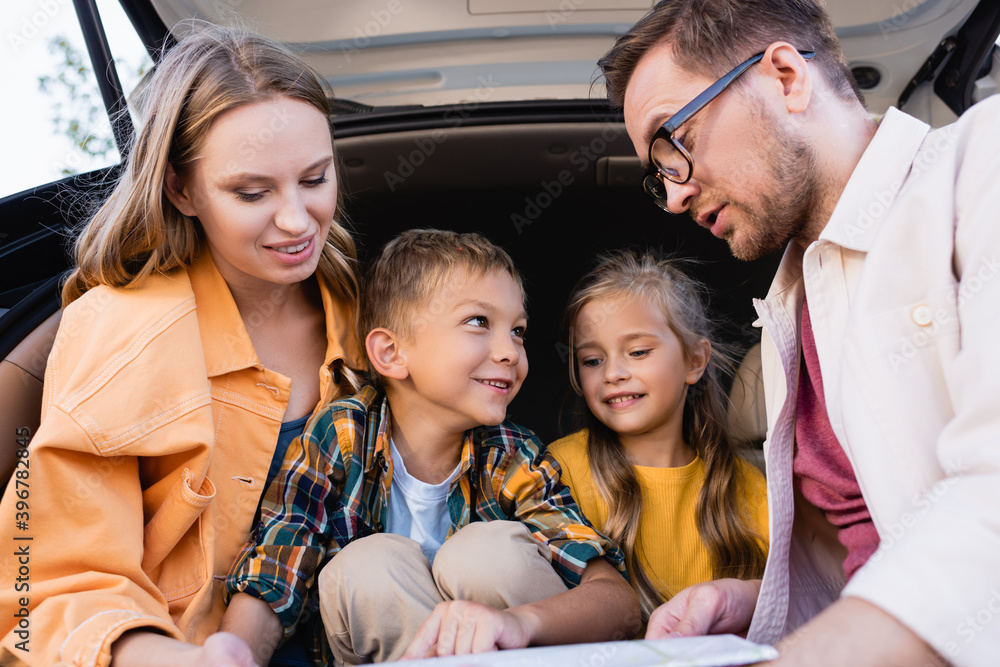 Cheerful family looking at map on blurred foreground near car trunk Cheerful family looking at map on blurred foreground near car trunk