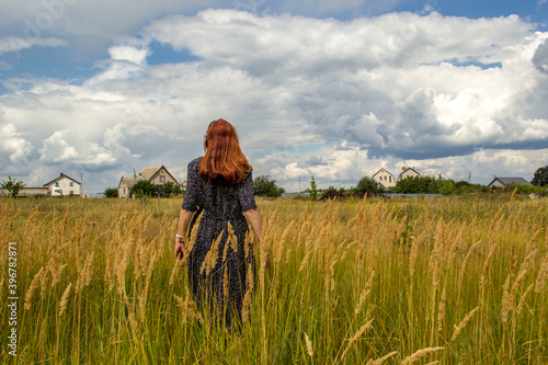  woman walking in a field on a summer day, sky with clouds over the field