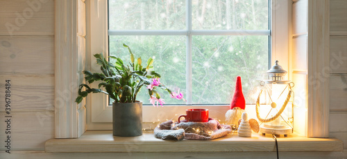 Christmas lantern, Angel, Christmas gnome, Christmas Cactus and red mug on the window of a wooden house overlooking the winter garden. photo