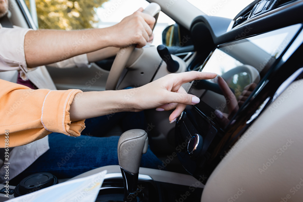 Cropped view of woman using audio system in car while husband driving on blurred background