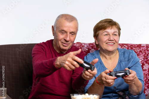 Senior couple playing at home, sitting on the couch a video game. Concept time during quarantine.