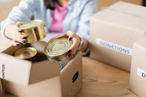 Принти на полотні Cropped view of woman holding canned food near carton box in charity center on b