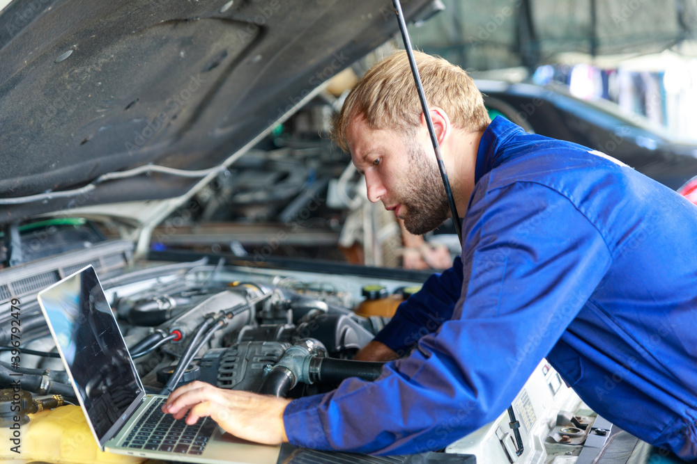 A Russian Male mechanic with tablet pc computer making system diagnostic in car at workshop. car service, repair, technology, maintenance and people concept A Russian Male mechanic with tablet pc computer making system diagnostic in car at workshop. car service, repair, technology, maintenance and people concept