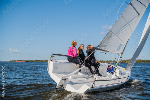 A beautiful white yacht is sailing in the wind on the river against the background of a beautiful autumn forest. A guy on board with two girls