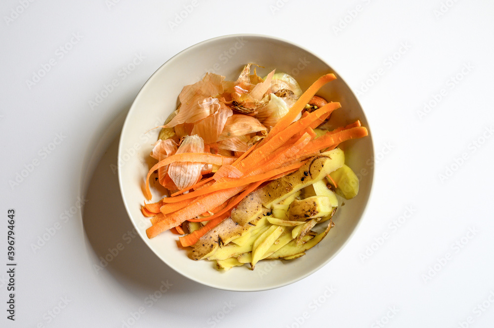 food waste from domestic kitchen, cleaning from vegetables onions potatoes and carrots in a plate on a white table background. sorting of household food waste food waste from domestic kitchen, cleaning from vegetables onions potatoes and carrots in a plate on a white table background. sorting of household food waste