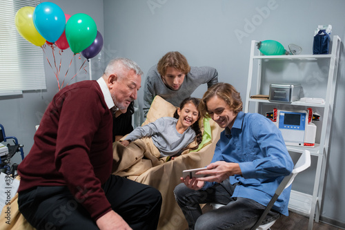 A little girl celebrating her birthday in a hospital ward with her family, they are having a video call with someone who could not make it to the party.