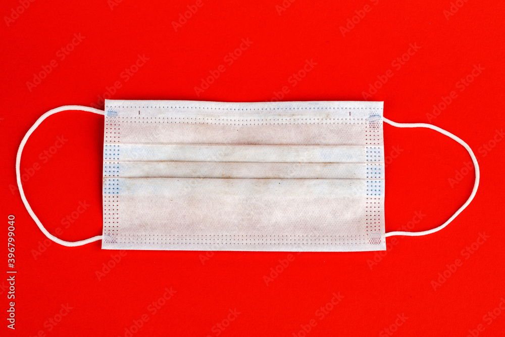 Dirty medical mask, medical protective mask isolated on red background. A disposable surgical mask covers the mouth and nose. Environmental pollution. Dirty medical mask, medical protective mask isolated on red background. A disposable surgical mask covers the mouth and nose. Environmental pollution.
