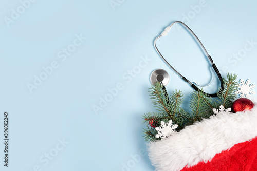 Medical stethoscope and christmas decorations in Santa Claus red bag on blue background. medical winter greeting card. Top view, flat lay, copy space photo