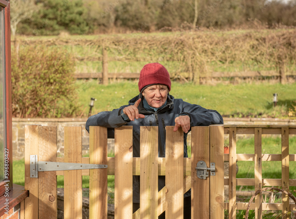 Senior woman pointing and laughing leaning over a wooden gate outdoors Senior woman pointing and laughing leaning over a wooden gate outdoors
