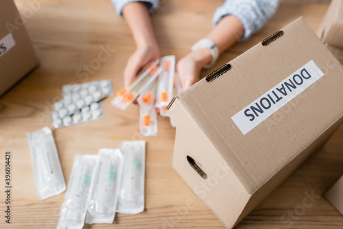 Cropped view of box with donations lettering and volunteer holding syringes near pills on blurred background © LIGHTFIELD STUDIOS