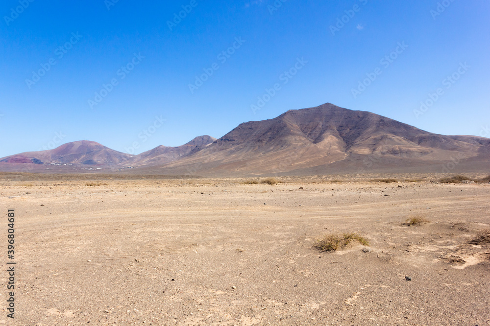 Empty desert volcanic landscape on sunny day in Lanzarote with mountains on background. No vegetationon on arid land in Canary Islands. Travel adventure concept