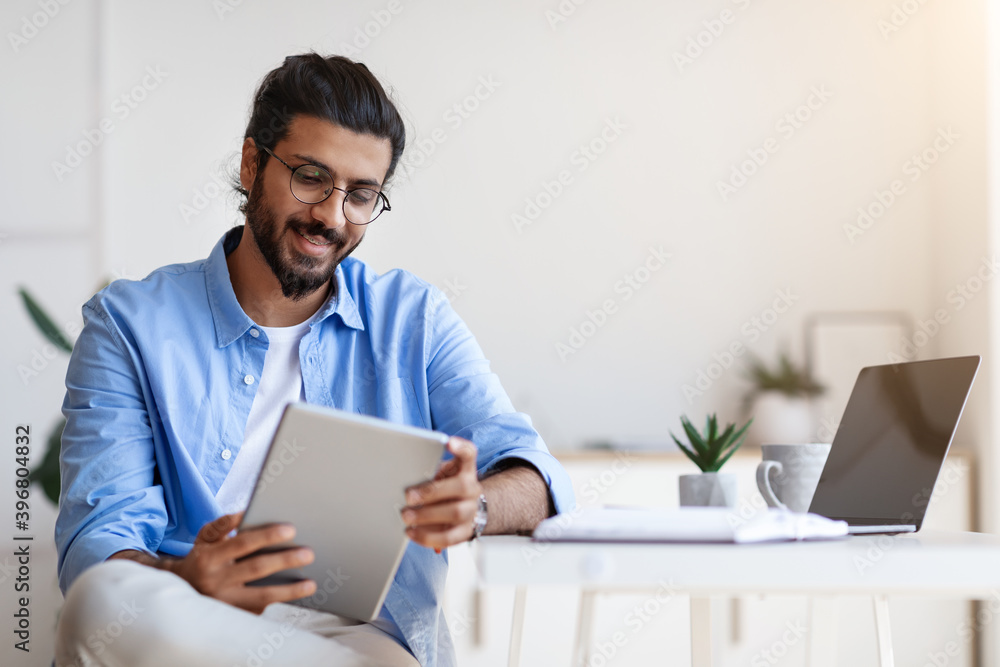 Indian Freelancer Guy Using Digital Tablet At Home, Having Break In Work Indian Freelancer Guy Using Digital Tablet At Home, Having Break In Work