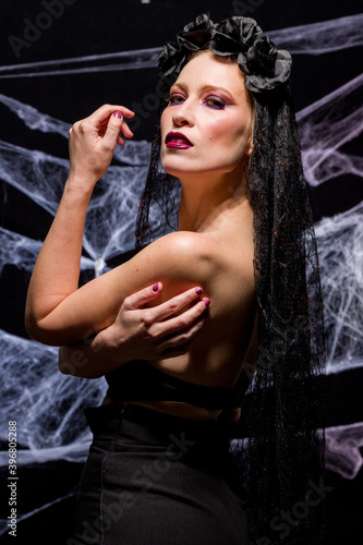 Woman dressed in elegant way as witch for Halloween party with black background and spider webs