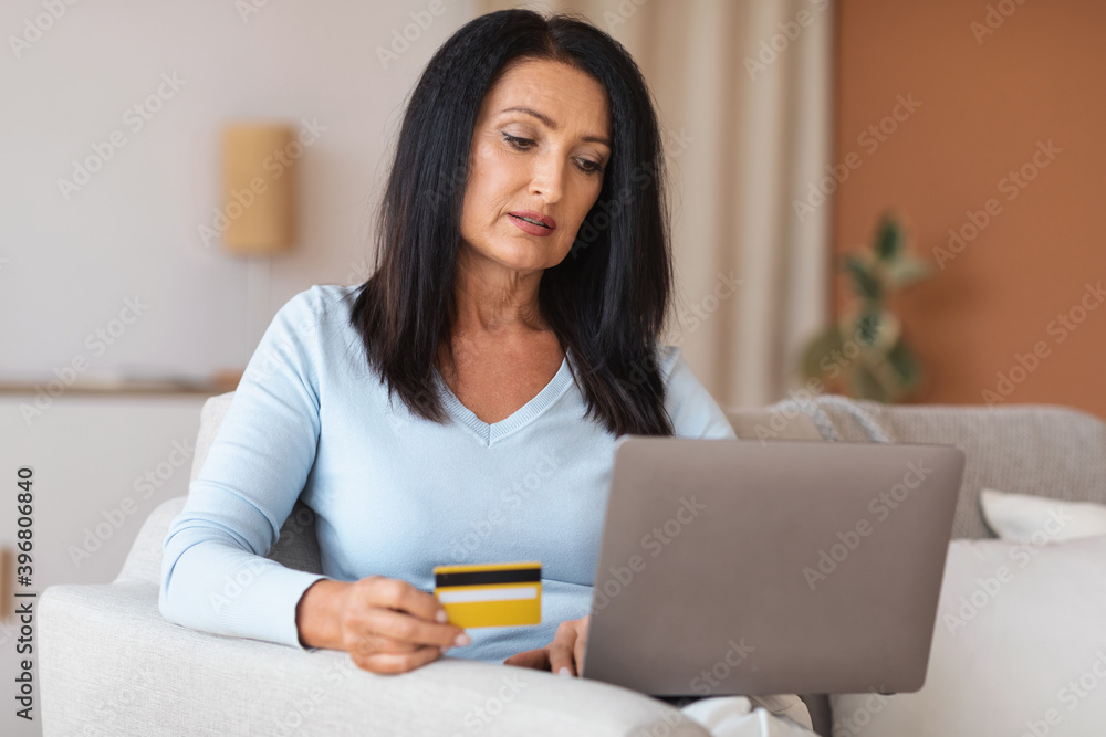 Mature woman making purchases using laptop holding credit card Mature woman making purchases using laptop holding credit card