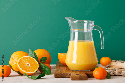 Fototapeta Naklejka Na Ścianę i Meble -  Freshly squeezed orange juice in a glass pitcher and fresh fruits with leaves, healthy drink, vitamin c concept, front view, copy space for a text