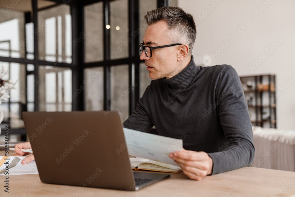 Focused man working with laptop and papers while sitting at table Focused man working with laptop and papers while sitting at table