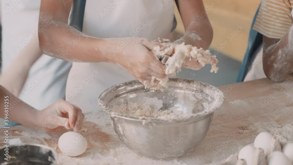 Close-up of hands of unrecognizable children kneading dough in metallic bowl, one kid trying to pull off spoon Close-up of hands of unrecognizable children kneading dough in metallic bowl, one kid trying to pull off spoon