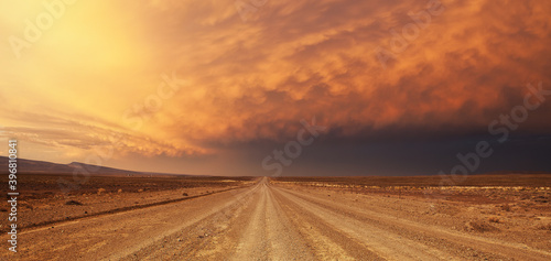 Photography A wide angle view of a huge thunder storm building over a lone dirt road in the