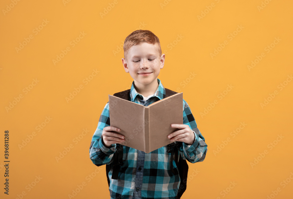 Obraz premium Joyful schoolboy reading book, yellow studio background