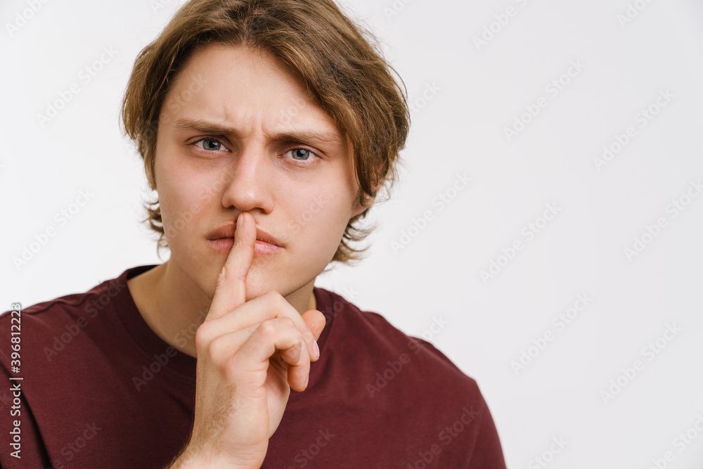 Serious young man showing silence gesture isolated Serious young man showing silence gesture isolated