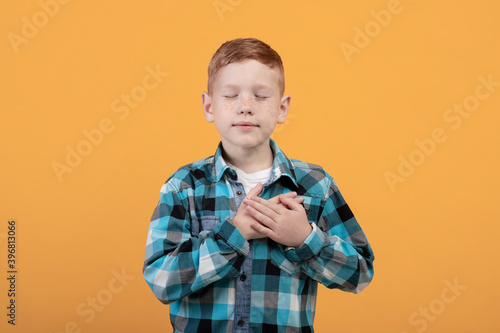 Adorable redhead boy with eyes closed holding hands on heart