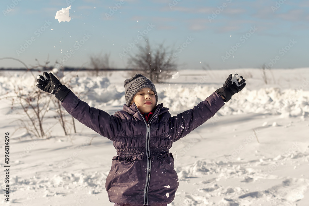 Happy little girl is playing with snow in park on white snow background