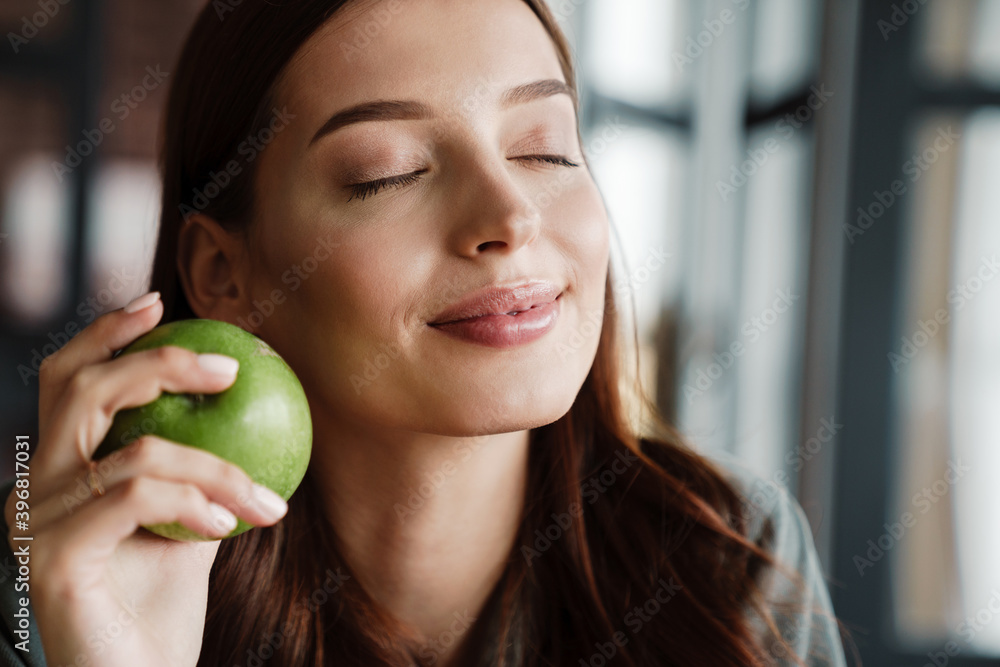 Beautiful happy nice woman smiling at camera while eating apple Beautiful happy nice woman smiling at camera while eating apple