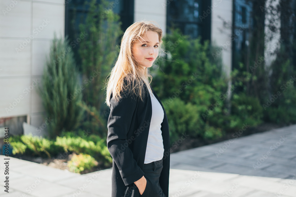 a cute blonde in a business black suit walks around the territory of a business center
a cute blonde in a business black suit walks around the territory of a business center