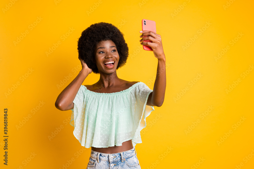 Photo portrait of woman closing mouth with one finger holding phone in hand looking at blank space isolated on vivid yellow colored background Photo portrait of woman closing mouth with one finger holding phone in hand looking at blank space isolated on vivid yellow colored background