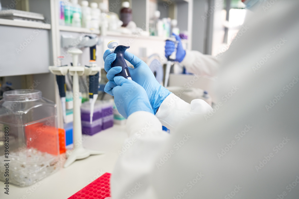 Scientist in rubber glove preparing pipette in laboratory Scientist in rubber glove preparing pipette in laboratory