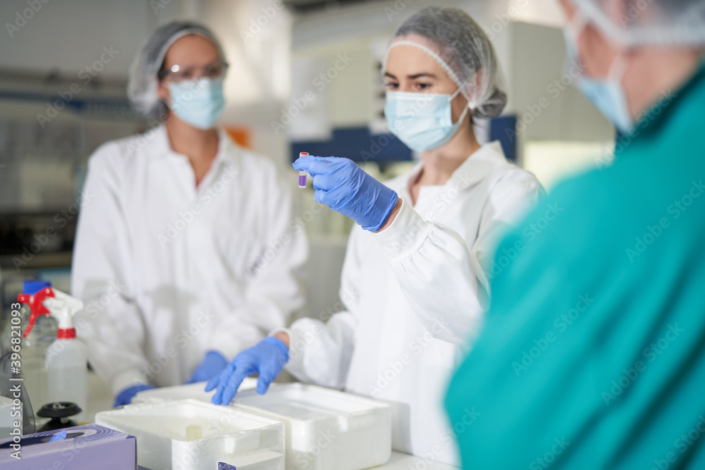 Female scientists in protective workwear examining specimen Female scientists in protective workwear examining specimen
