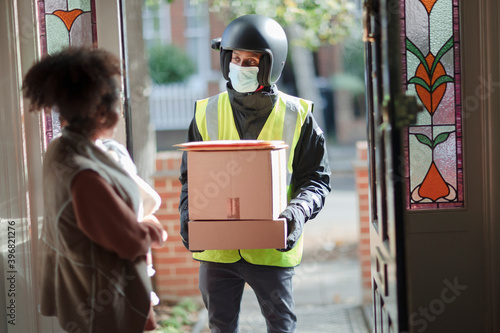 Woman receiving packages from delivery man in face mask at front door photo