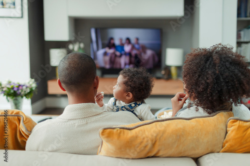 Parents and baby daughter watching TV on living room sofa