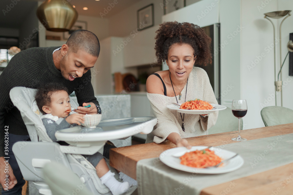 Couple eating spaghetti and feeding baby daughter at dining table