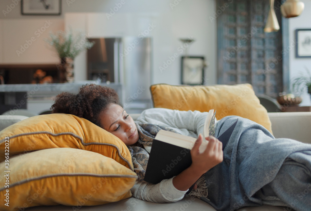 Woman relaxing and reading book on living room sofa Woman relaxing and reading book on living room sofa