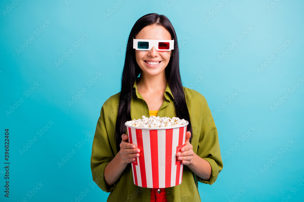 Photo of cheerful cute lady hold big paper box popcorn toothy smile wear 3d glasses green shirt isolated blue color background Photo of cheerful cute lady hold big paper box popcorn toothy smile wear 3d glasses green shirt isolated blue color background
