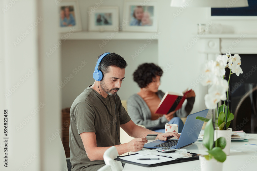 Man with headphones and credit card paying bills at laptop Man with headphones and credit card paying bills at laptop