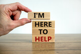 Here to help symbol. Male hand builds stack from blocks with words 'i am here to help'. Wooden table. Beautiful white background. Copy space. Business and here to help concept.