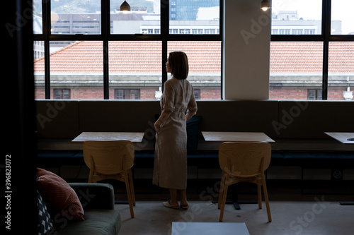 Asian woman looking out of window in creative office cafeteria